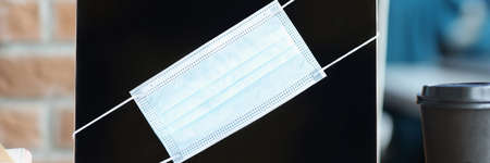 Protective medical mask hanging on laptop screen closeup