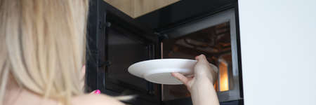 Woman putting plate of food in open microwave closeupの写真素材