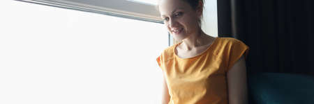 Young woman sitting on windowsill and typing on laptop keyboard