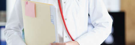 Woman doctor in white coat and stethoscope holds medical documents in her handの写真素材