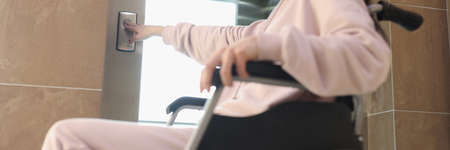 Smiling woman in wheelchair presses button of elevatorの写真素材