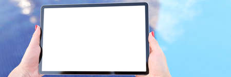 Female hands hold tablet with blank white screen above pool water