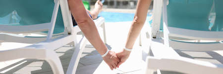 Man and woman lying on sun loungers near pool and holding hands closeupの写真素材