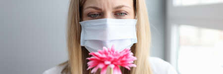 Woman in protective medical mask sniffing flowerの写真素材
