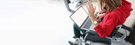 Disabled woman in wheelchair waving hand at laptop screenの写真素材