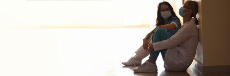 Tired women doctors are sitting in masks in corridorの写真素材