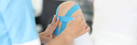 Rehabilitation therapist gluing blue tapes on woman knee closeupの写真素材