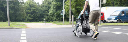 Man helping disabled woman to move in wheelchair on roadの写真素材