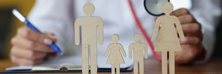 Doctor writing in medical documents and holding stethoscope in front of toy men closeupの写真素材