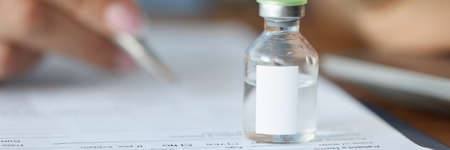Doctor holding glass jar of medicine in his hands and writing in documents closeupの写真素材