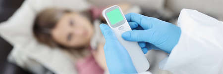 Doctor in gloves measuring temperature of woman with non contact thermometer at home closeup