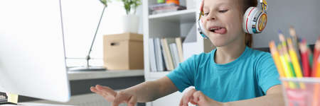 Little girl in headphones sitting at table and typing on computer keyboard