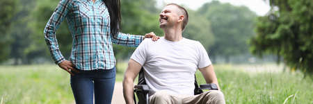 Smiling man in wheelchair walks in park with womanの写真素材