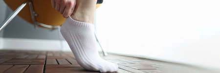 Woman puts on white short sock on her leg