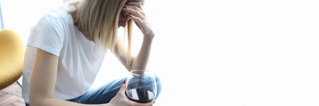Depressed woman sits with her head bowed and holds glass of wine