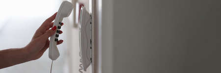 Woman hand picking up phone in hotel corridor closeup