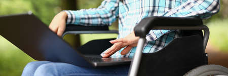 Woman in wheelchair on her knees with laptopの写真素材