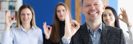 Businessman showing ok gesture on background of colleagues in office