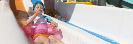 Little girl in swimming circle and father riding roller coaster in water park