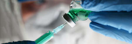 Doctor in protective suit and gloves is taking medicine from vial into syringeの写真素材