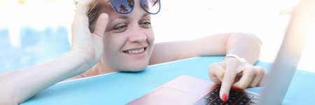 Young smiling woman is working on laptop while in poolの写真素材