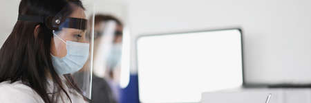 Women in protective screens working on laptops in office