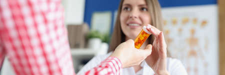 Woman doctor giving jar of capsules to patient in hands in clinic closeupの写真素材