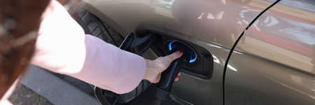 Woman inserting electric charger into car closeupの写真素材