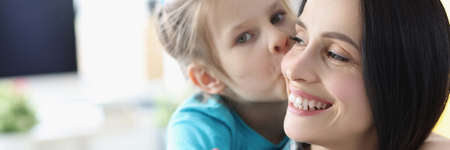 Little girl kissing smiling mom at homeの写真素材