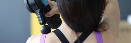 Woman doing massage of muscles of neck and back with percussion massager closeup