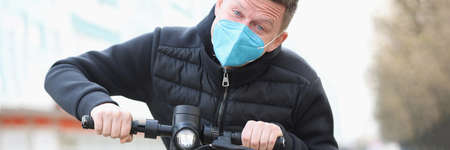 Man in protective medical mask riding electric scooter