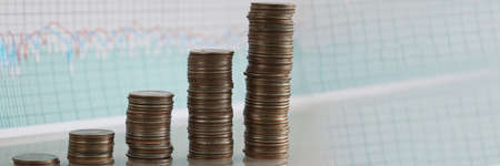 Stacks of coins increasing in row against background of financial indicators