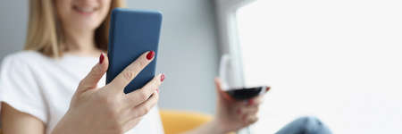 Woman holds smartphone and glass of red wine in her handsの写真素材