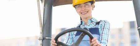 Smiling woman builder in helmet driving construction equipmentの写真素材