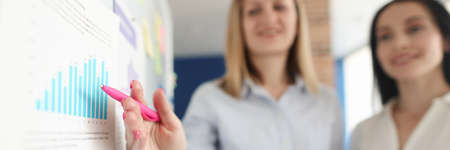 Business women standing at blackboard and showing pen on chart closeupの写真素材