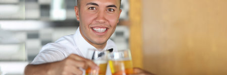 Portrait of young man holding glass of beer while clinking glasses with another glassの写真素材