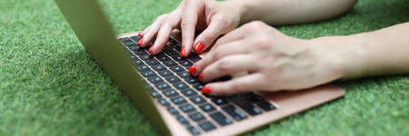 Woman lies on green lawn and works on laptop closeupの写真素材