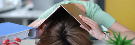 Tired young woman lies on table on head with laptopの写真素材