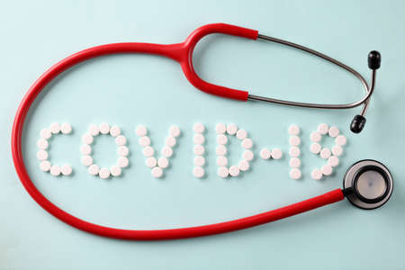 Red stethoscope lying near inscription from covid 19 tablets closeupの写真素材