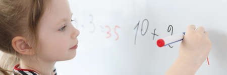Little girl solving math examples on blackboard