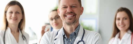 Successful smiling man doctor standing against background of colleagues in clinicの写真素材