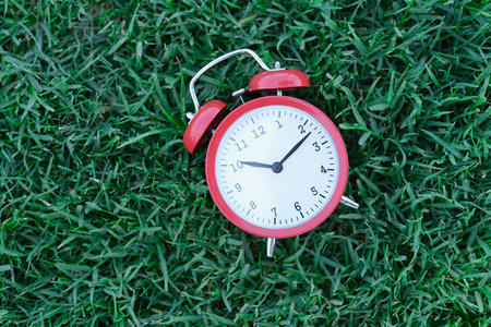 Red classic alarm clock lying on green grass closeupの写真素材