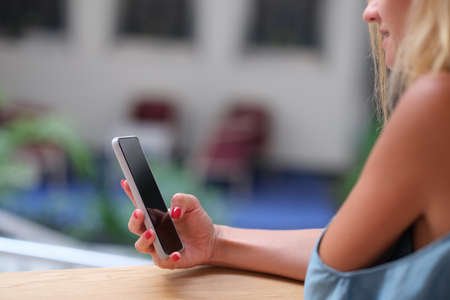 Young woman holding mobile phone in her hands and looking at screen closeup