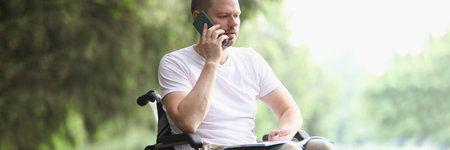 Disabled man in wheelchair talking on mobile phone in park