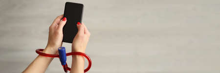 Woman with tied hands holding mobile phone closeupの写真素材