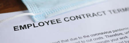 Termination of employment contract due to coronavirus pandemic, along with protective mask lies on tableの写真素材