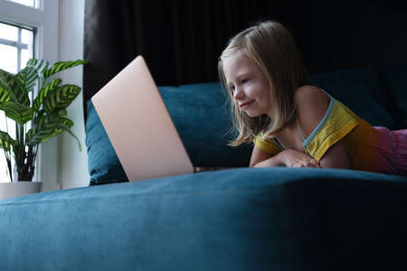 Little girl lying on couch and looking at laptop screenの写真素材