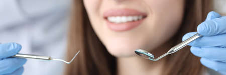 Dentist doctor holding dental instruments in front of female patient in clinic closeup