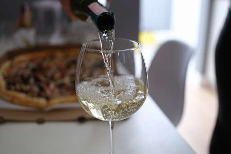 White wine pouring from bottle into glass goblet on pizza background closeupの写真素材