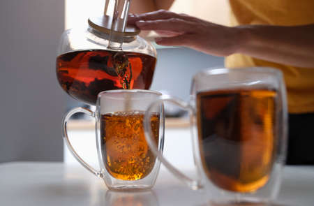 Woman pouring black tea from teapot into cup closeup